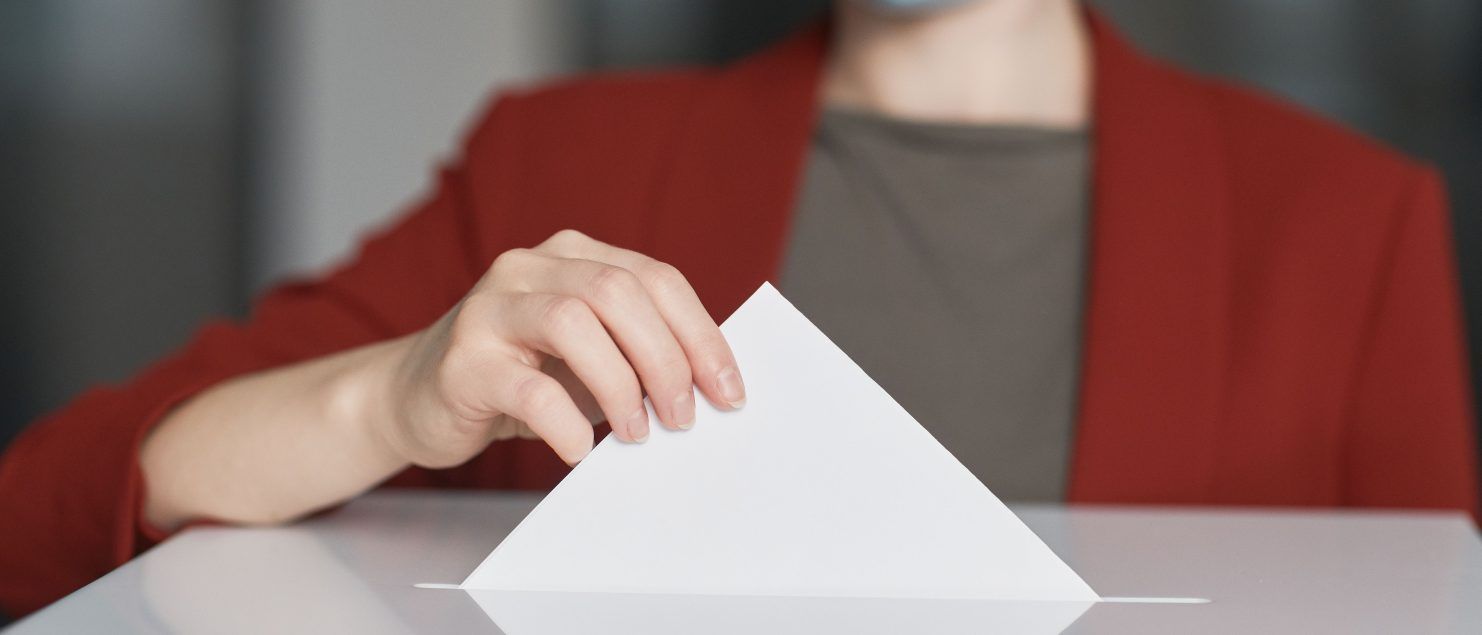 Persona depositando su papeleta en la urna de una mesa electoral en España, con los miembros de la mesa supervisando el proceso. Asesoramiento legal sobre obligaciones y excusas electorales por Montero de Cisneros Abogados.